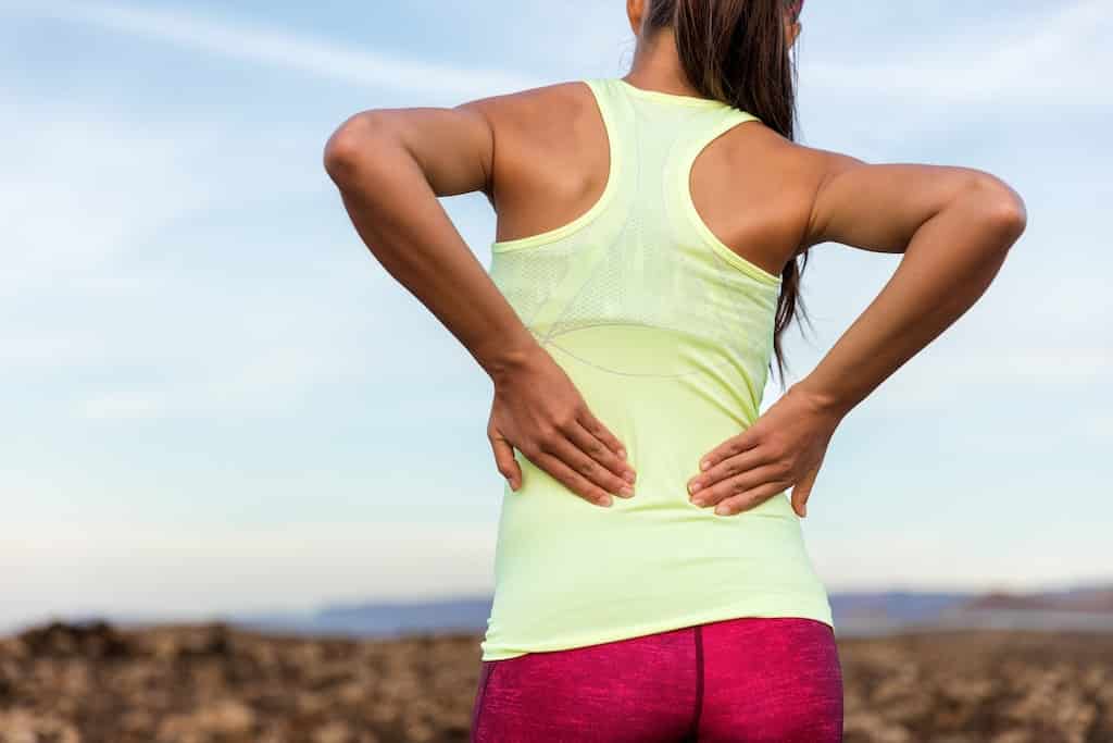 Woman in athletic clothes holding her back in pain