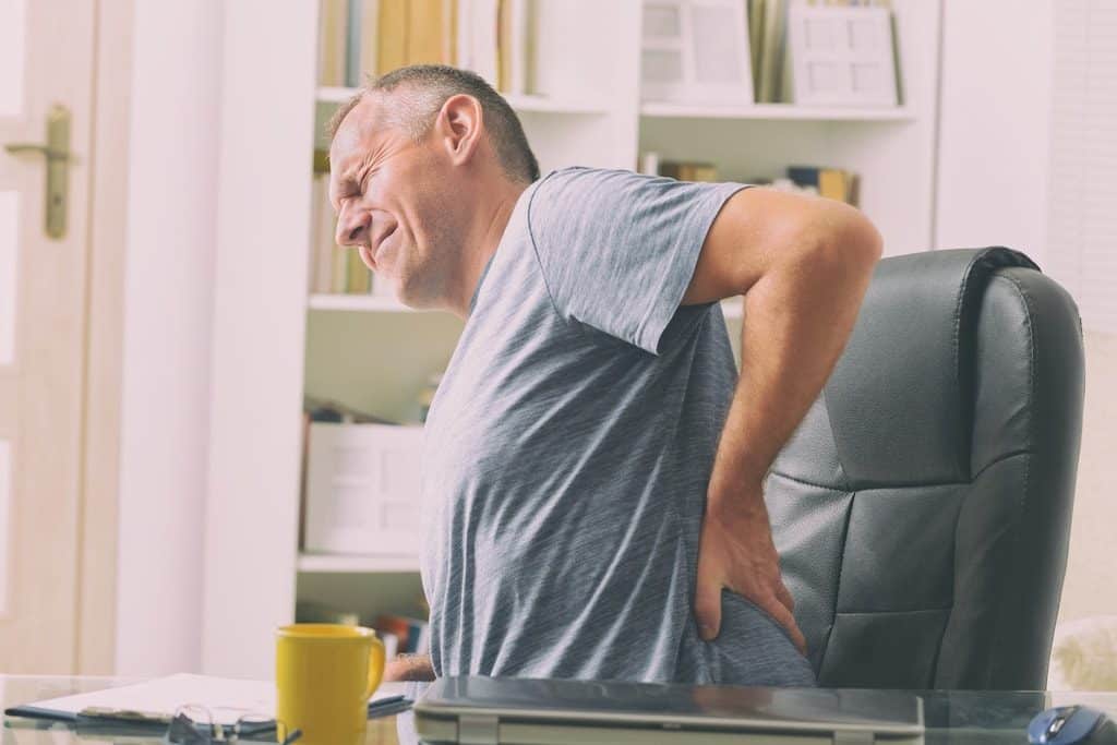 Man in a desk chair who appears to be in pain holding his lower back