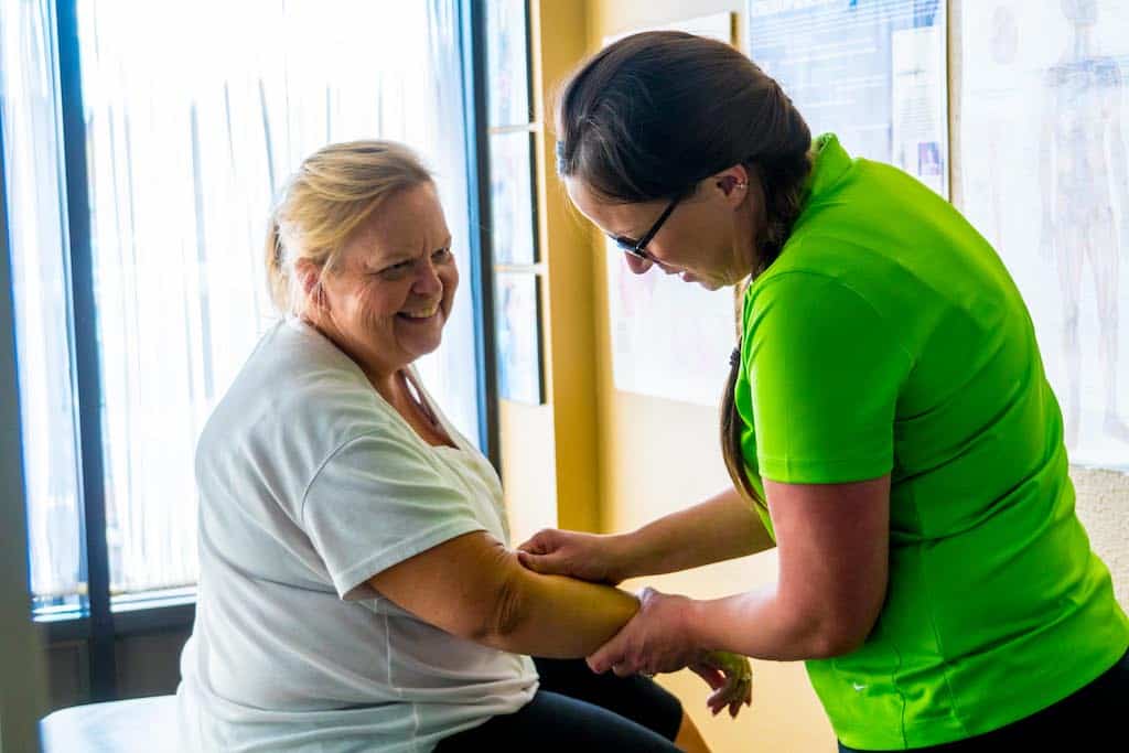 A practicioner helping a smiling female patient by massaging her arm