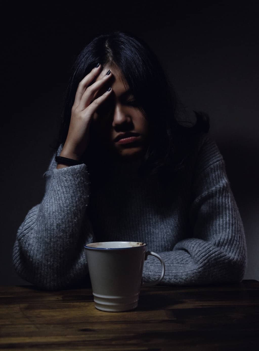 Photo of a woman with a mug of coffee holding her forehead in pain