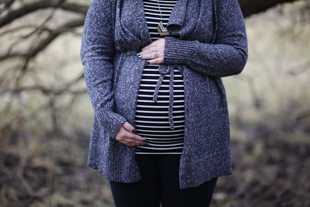 Photo of a woman in a blue cardigan holding her pregnant belly