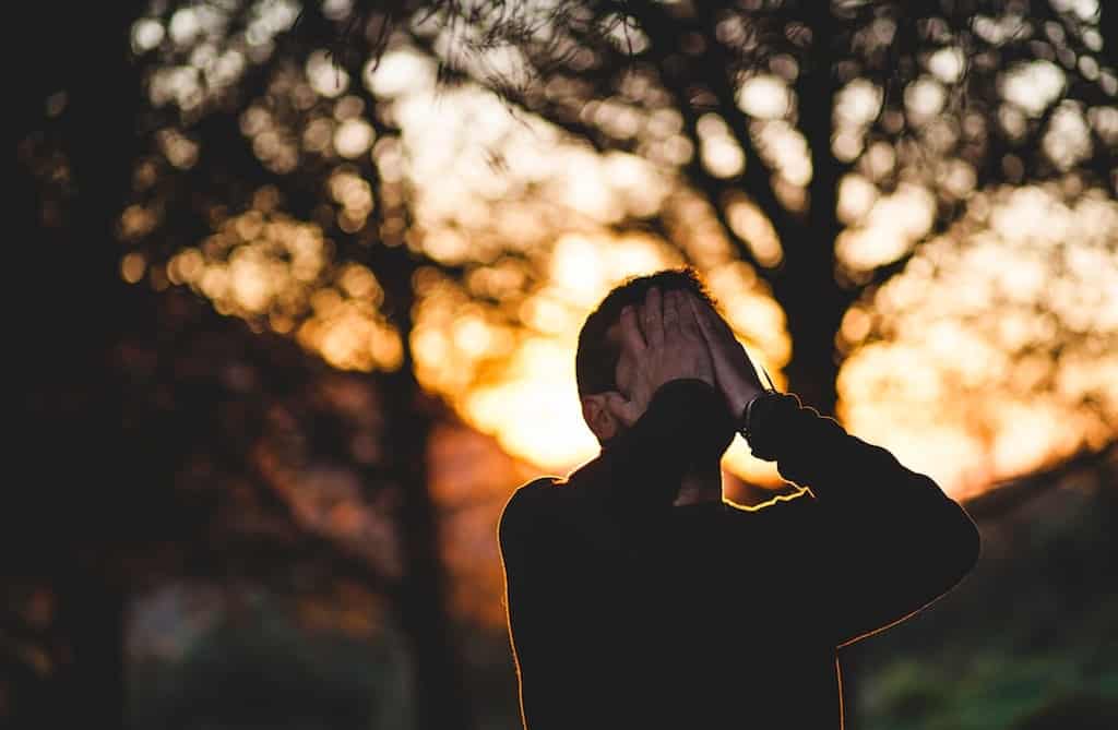 Photo of a man in front of a sunset with his hands over his face
