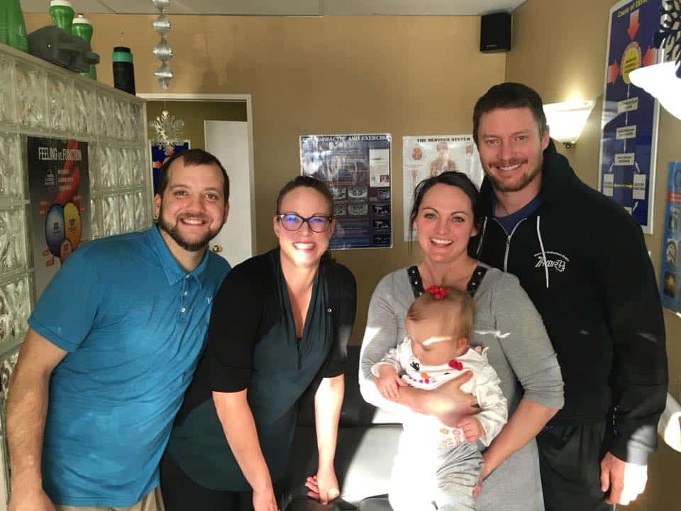 Four smiling adults standing in a treatment room while holding a baby