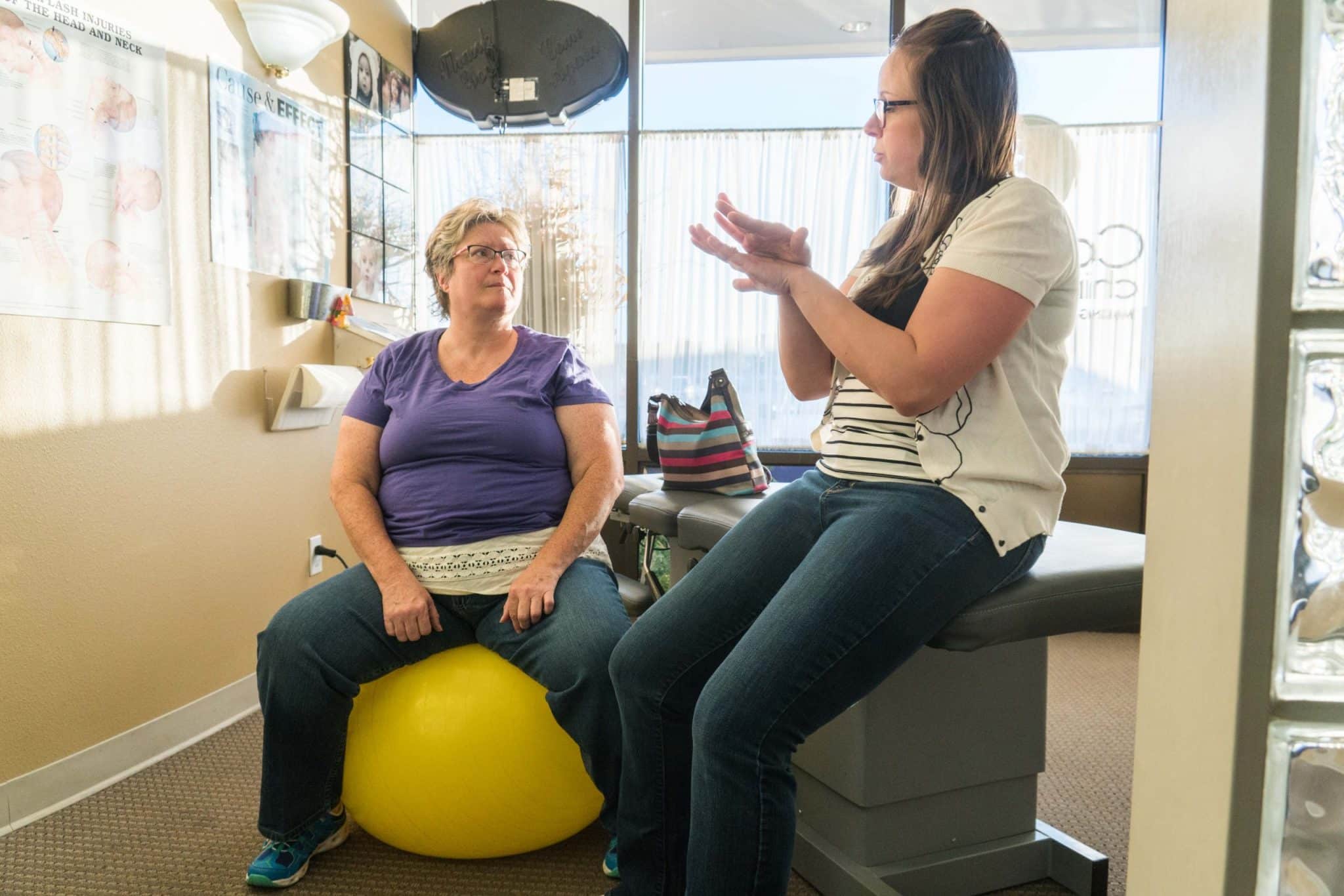 A practicioner guiding a female patient through exercises on an exercise ball